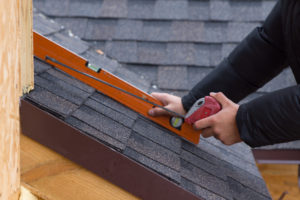 Photo: roofer holding a tape measure and level over newly installed roofing tiles