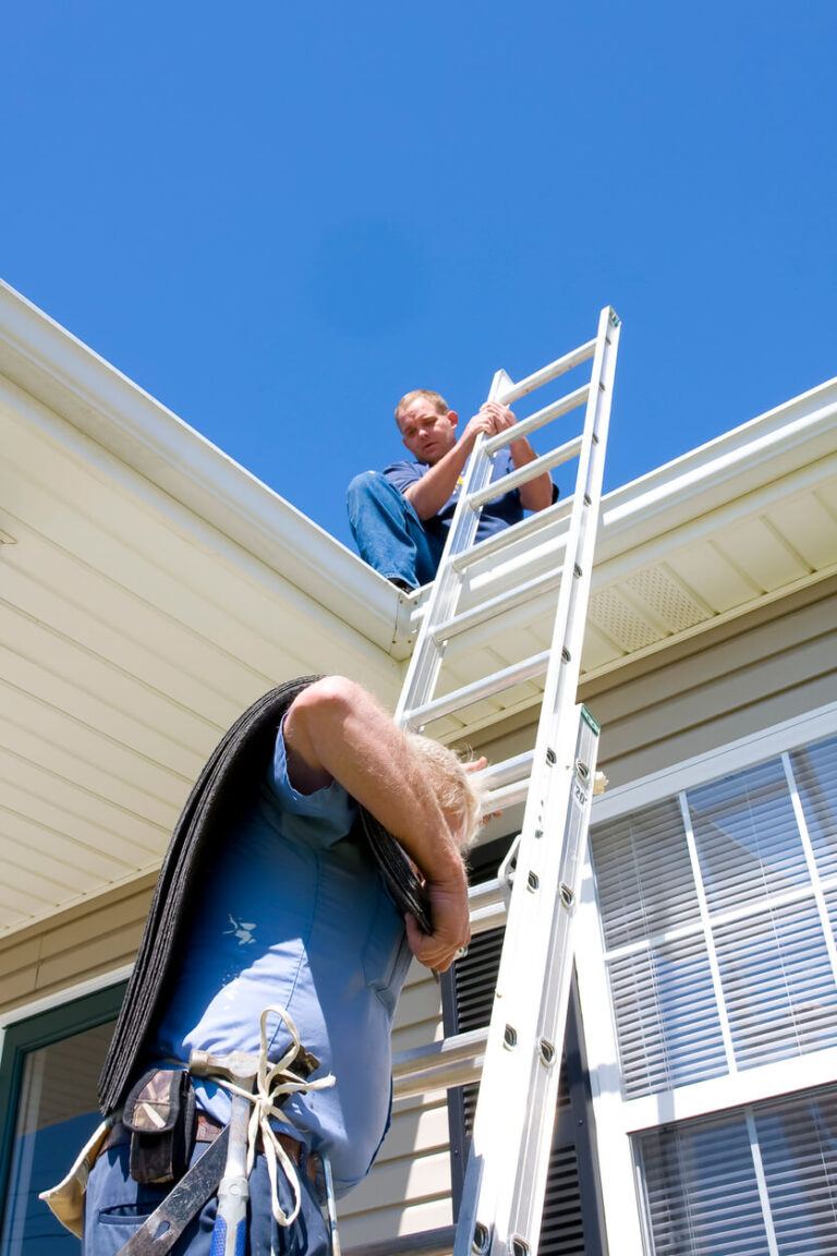 Photo: Man holding ladder for roofing crew member